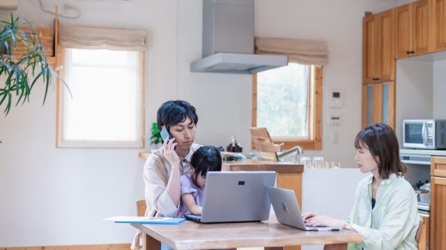 自宅でPC作業をする夫婦と遊ぶ子ども｜共働き世帯のイメージ
